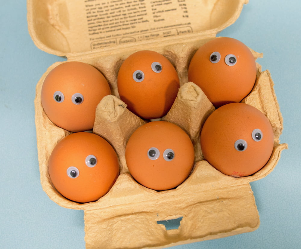 a dozen eggs with googly eyes in a cardboard box