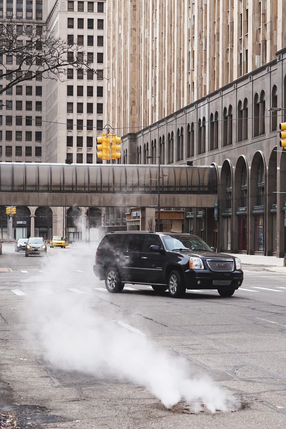 black SUV on road and white smoke coming from manhole during daytime