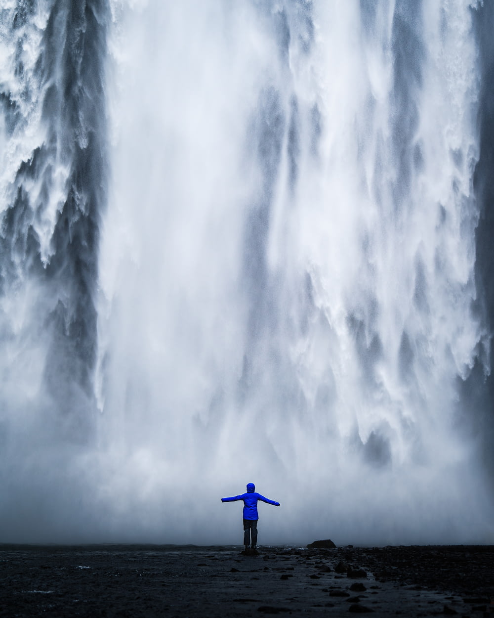 Person in blauer Jacke steht vor Wasserfällen