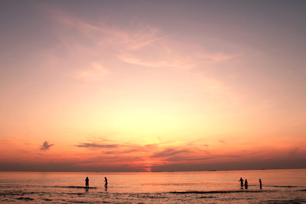silhouette di persone in piedi in riva al mare durante l'ora d'oro