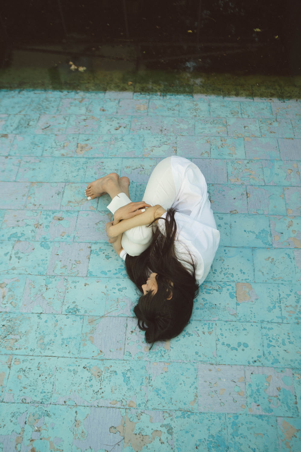woman wearing white collared button-up long-sleeved shirt and pants lying on green concrete pavement