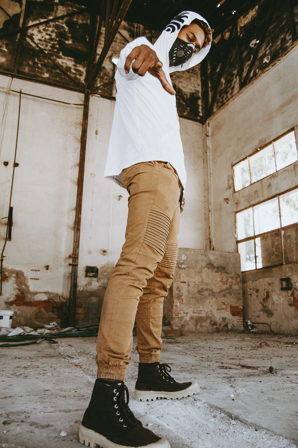man wearing white hoodie and brown skinny jeans standing inside abandoned building