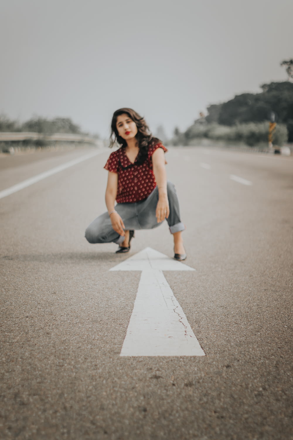 woman in red dotted shirt and gray denim pants on road with arrow
