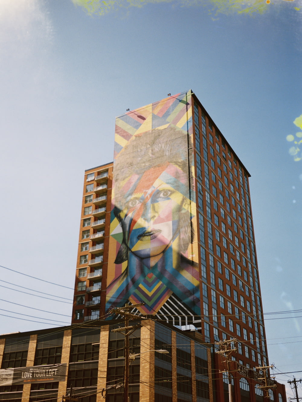 brown high-rise building with multicolored woman graphic painting under blue and white skies during daytime