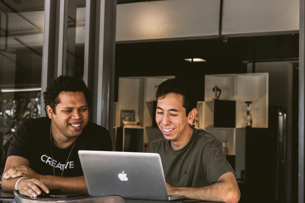 zwei lächelnde Männer, die auf das MacBook schauen