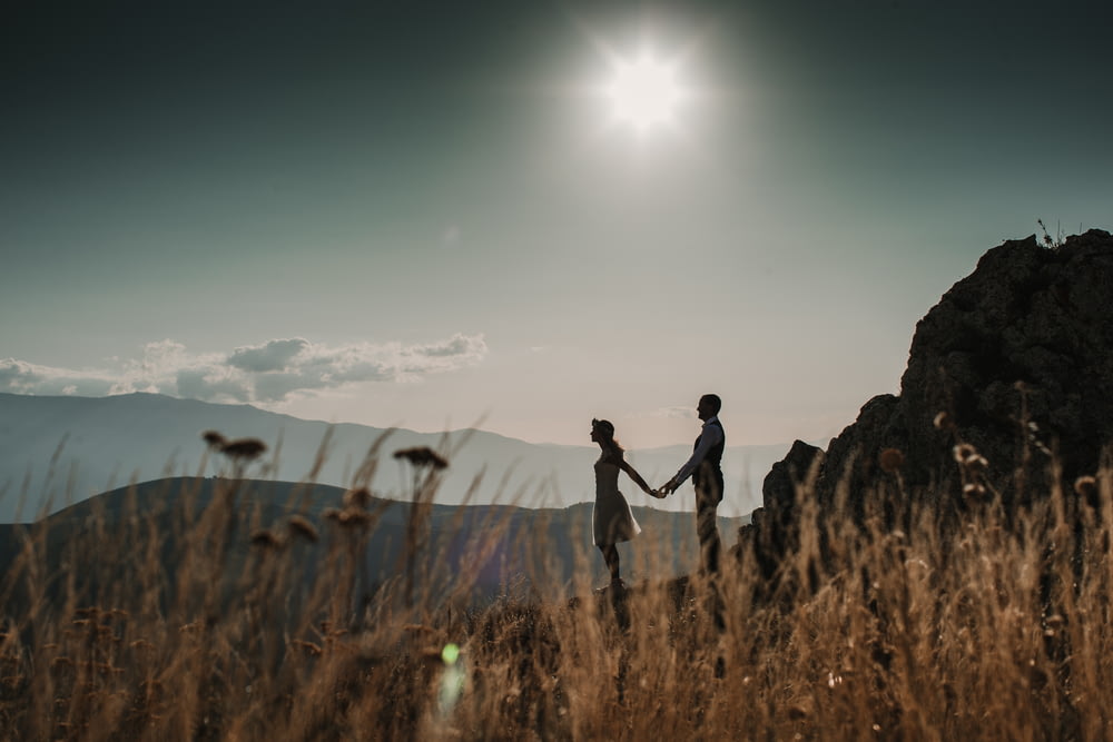 a couple holding hands while standing on top of a mountain