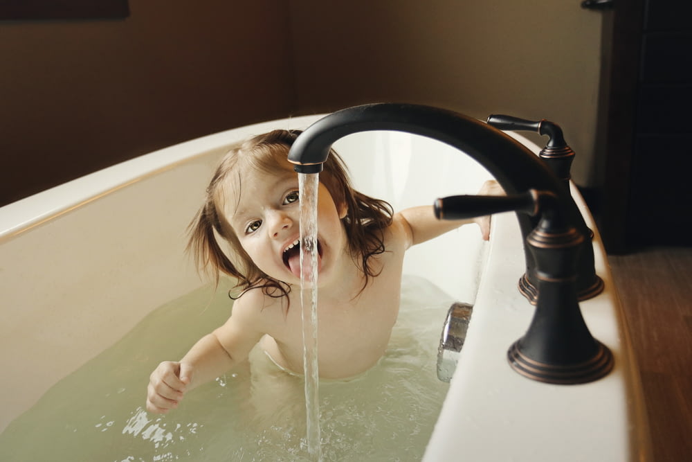 Mädchen in der Badewanne probiert Wasser aus schwarzem Wasserhahn