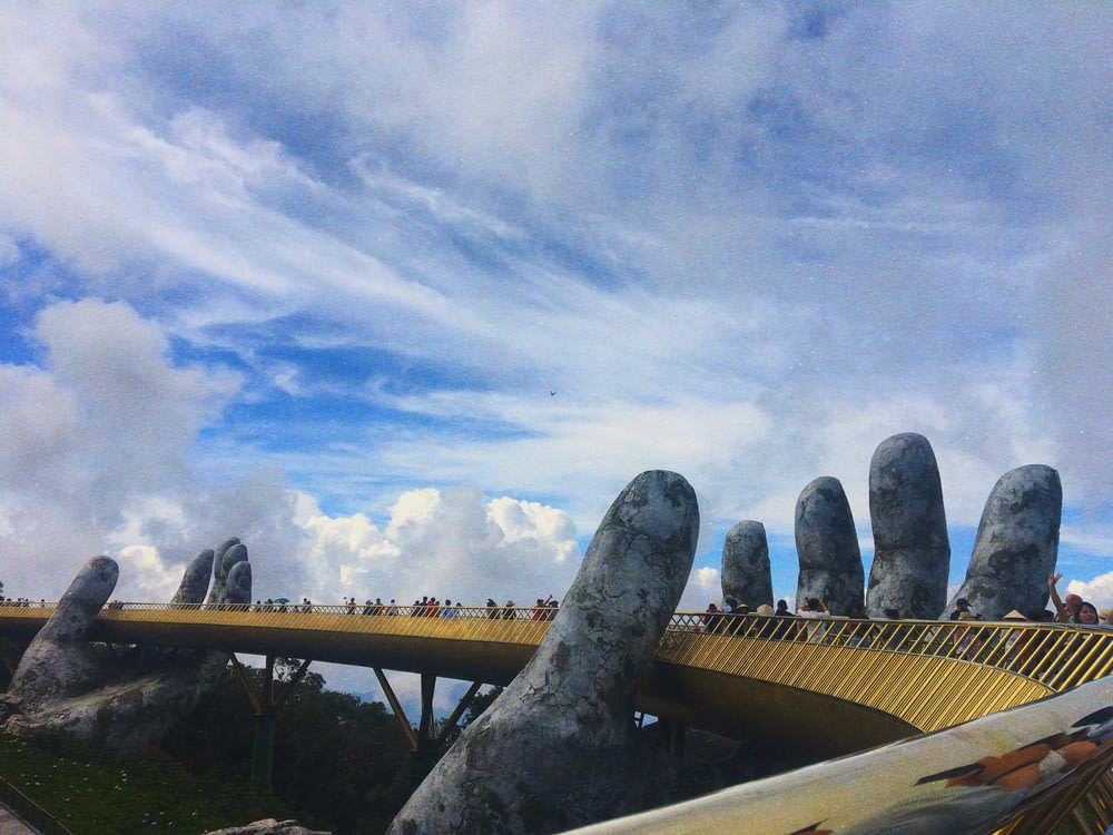 people walking on bridge with human hands sculpture during day