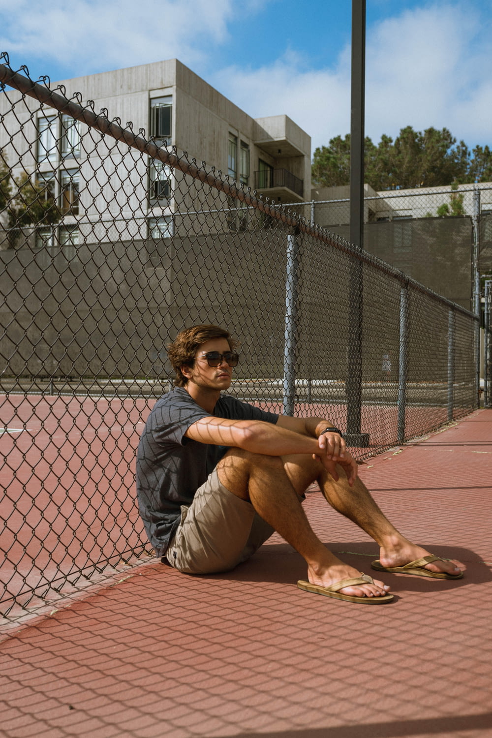 man wearing black crew-neck t-shirt sitting and leaning against chain link fence