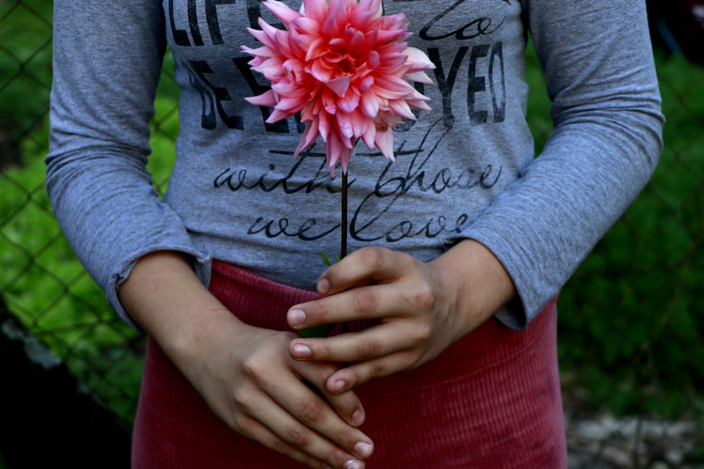 a woman holding a pink flower in her hands