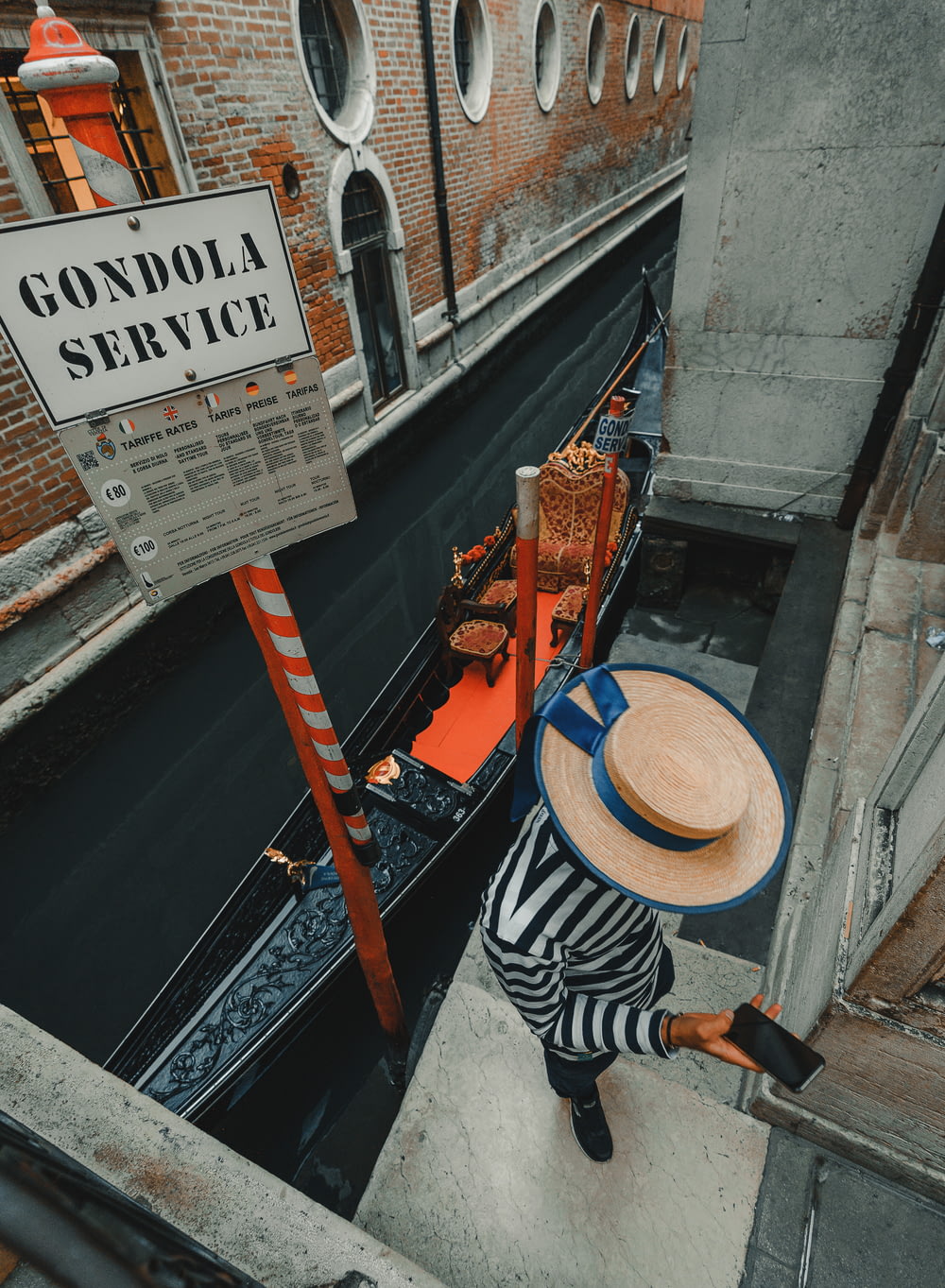 person using phone while standing near Gondola beside Venice canal during daytime
