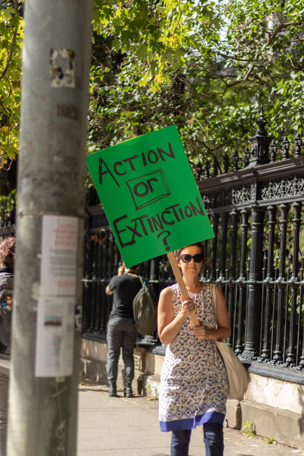 woman walking on sidewalk holding green action or extinction signboard