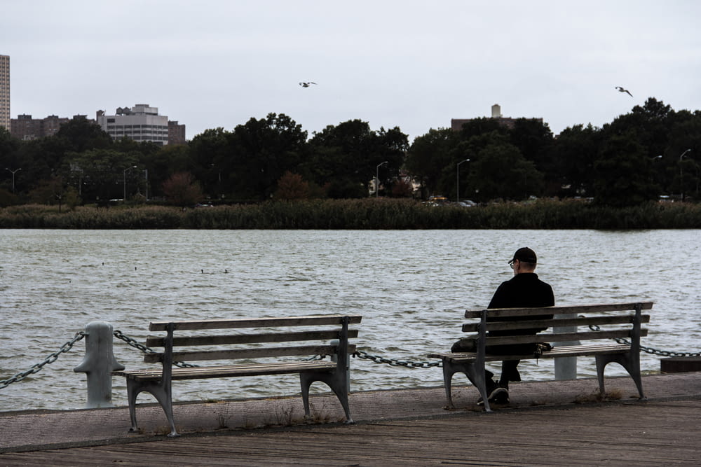 man sitting on bench beside body of water