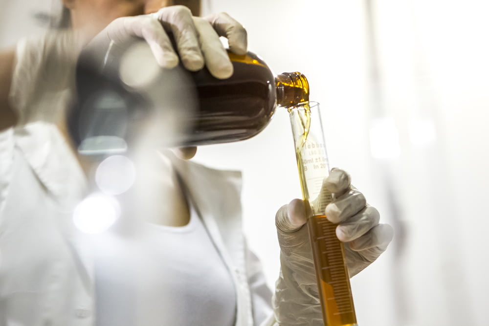 Frau in weißem Laborkittel mit brauner Flasche und Glasröhrchen