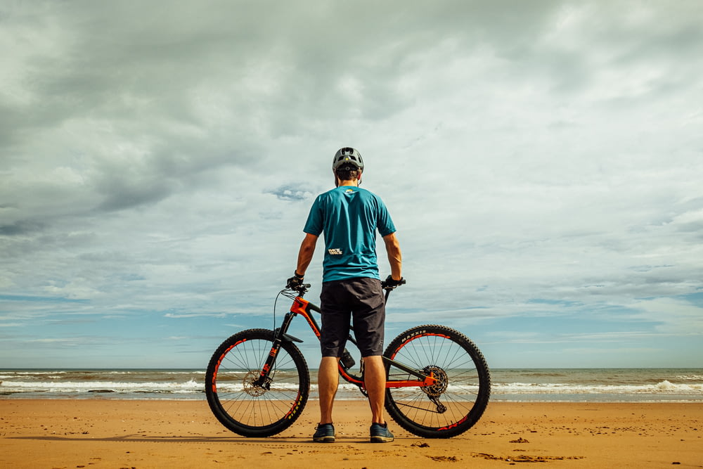 hombre de pie junto a la bicicleta en la orilla del mar