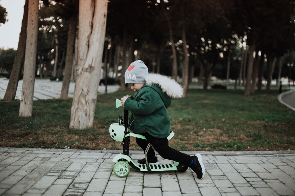 Un niño pequeño montando un scooter verde en una acera