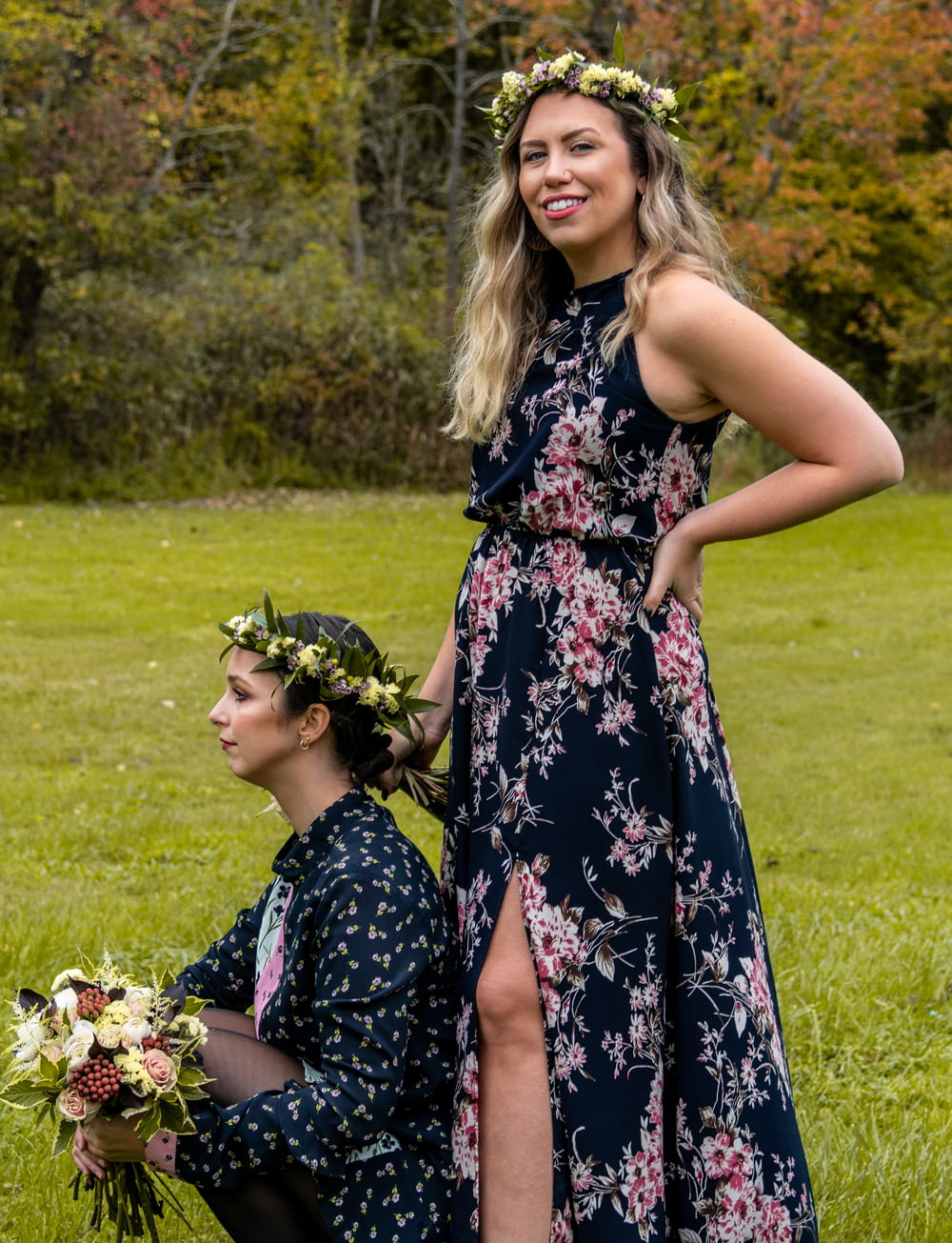 woman wearing floral maxi dress beside woman sitting on green grass field