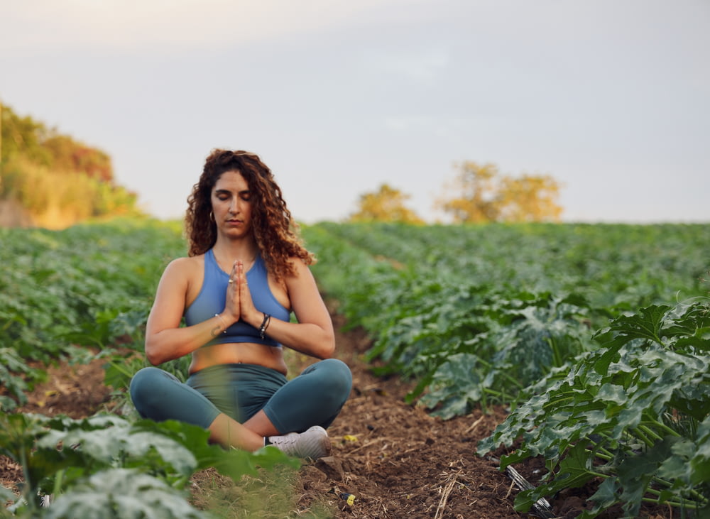 woman sitting on ground while meditating and surrounded by plant field in macro photography