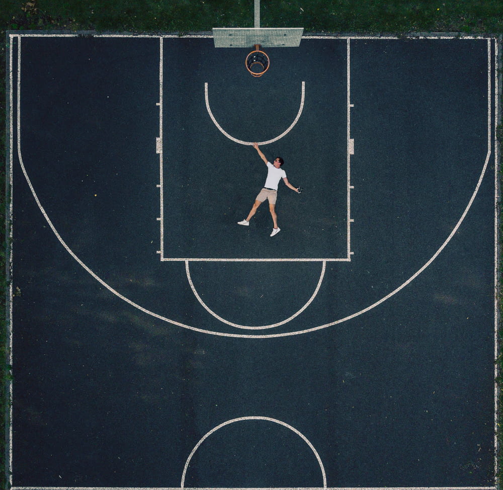 man in white shirt lying on outdoor basketball court