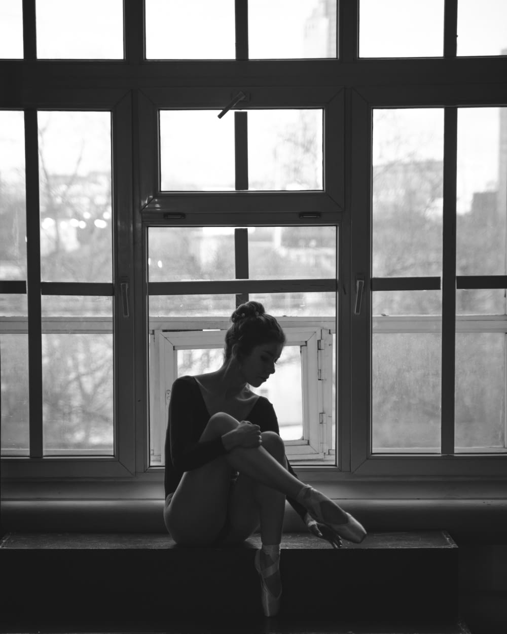 greyscale photography of woman beside window