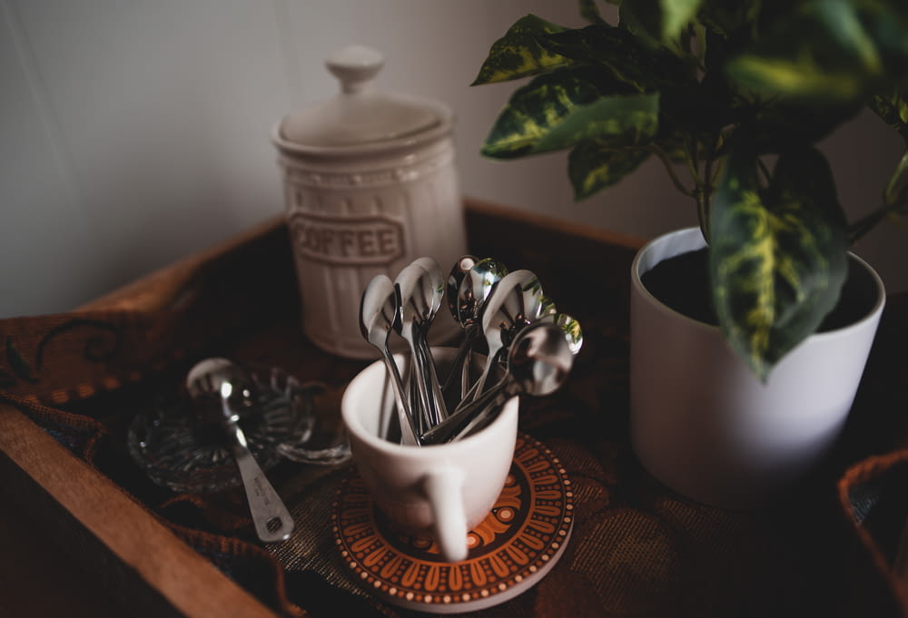 silverware in white ceramic mug beside coffee jar