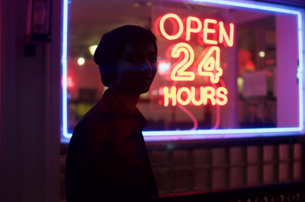Mann, der nachts neben einer offenen 24-Stunden-Beschilderung steht