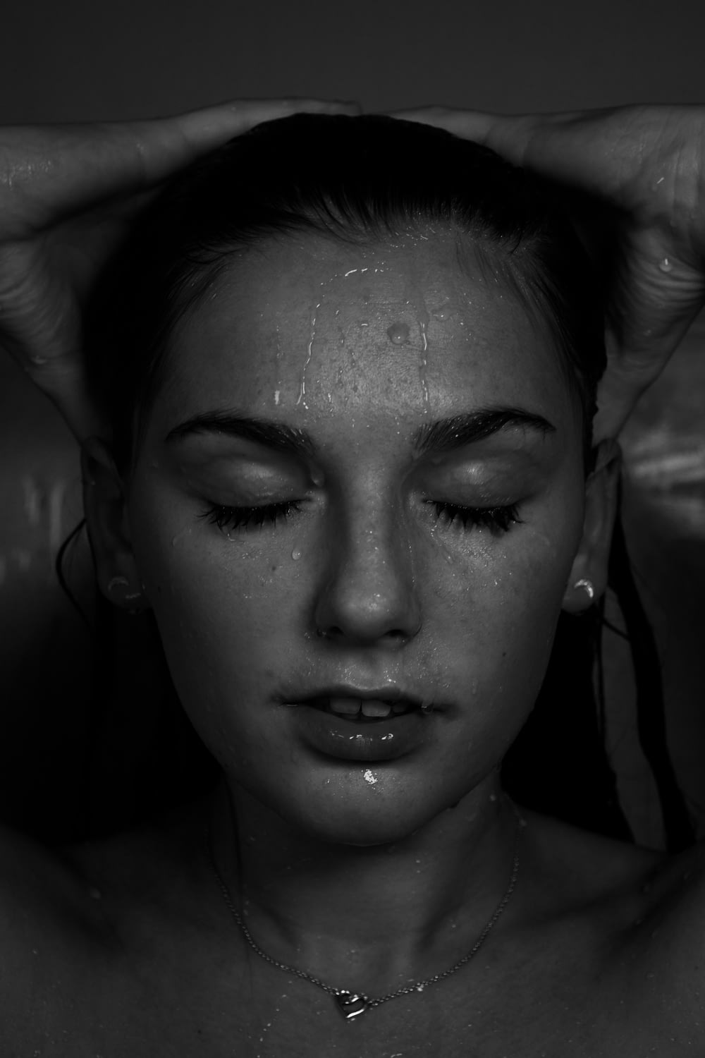 Photographie en niveaux de gris d’une femme aux seins nus avec des gouttes d’eau sur le visage