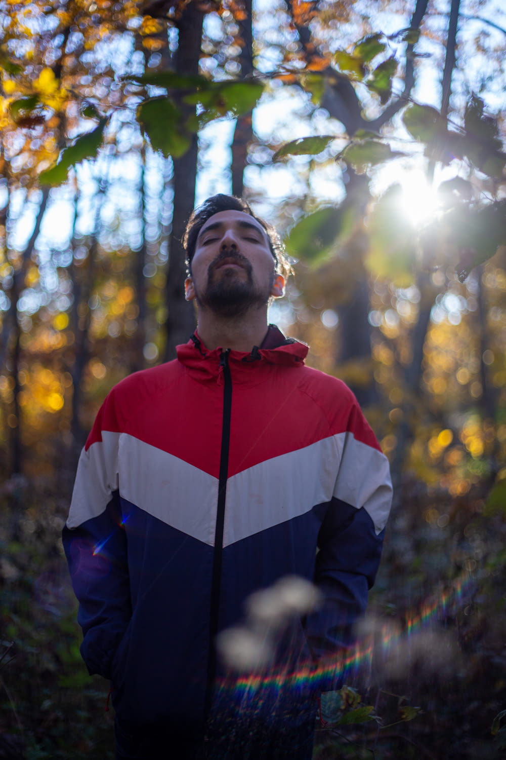 man in red, white, and blue zip-up jacket standing in forest