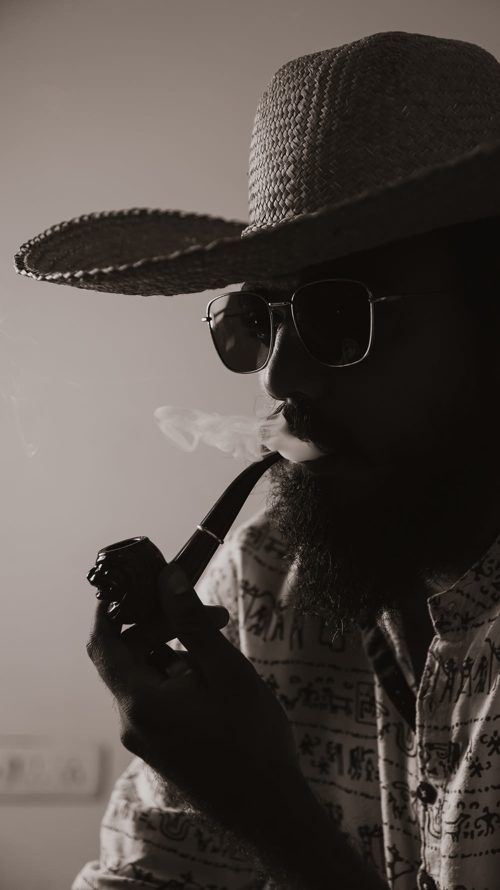 Un hombre con sombrero y gafas de sol fumando una pipa