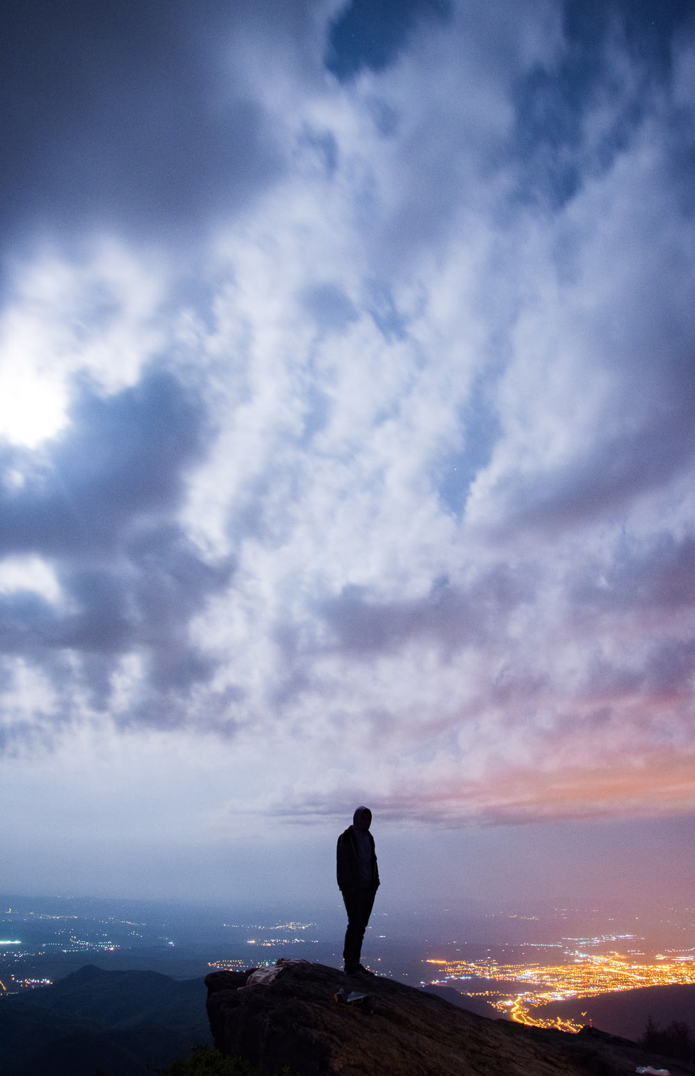 man standing on cliff with cityscape view under cloudy sky