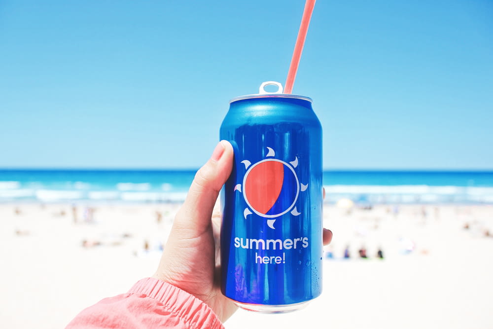 person holding Pepsi soda can on seashore