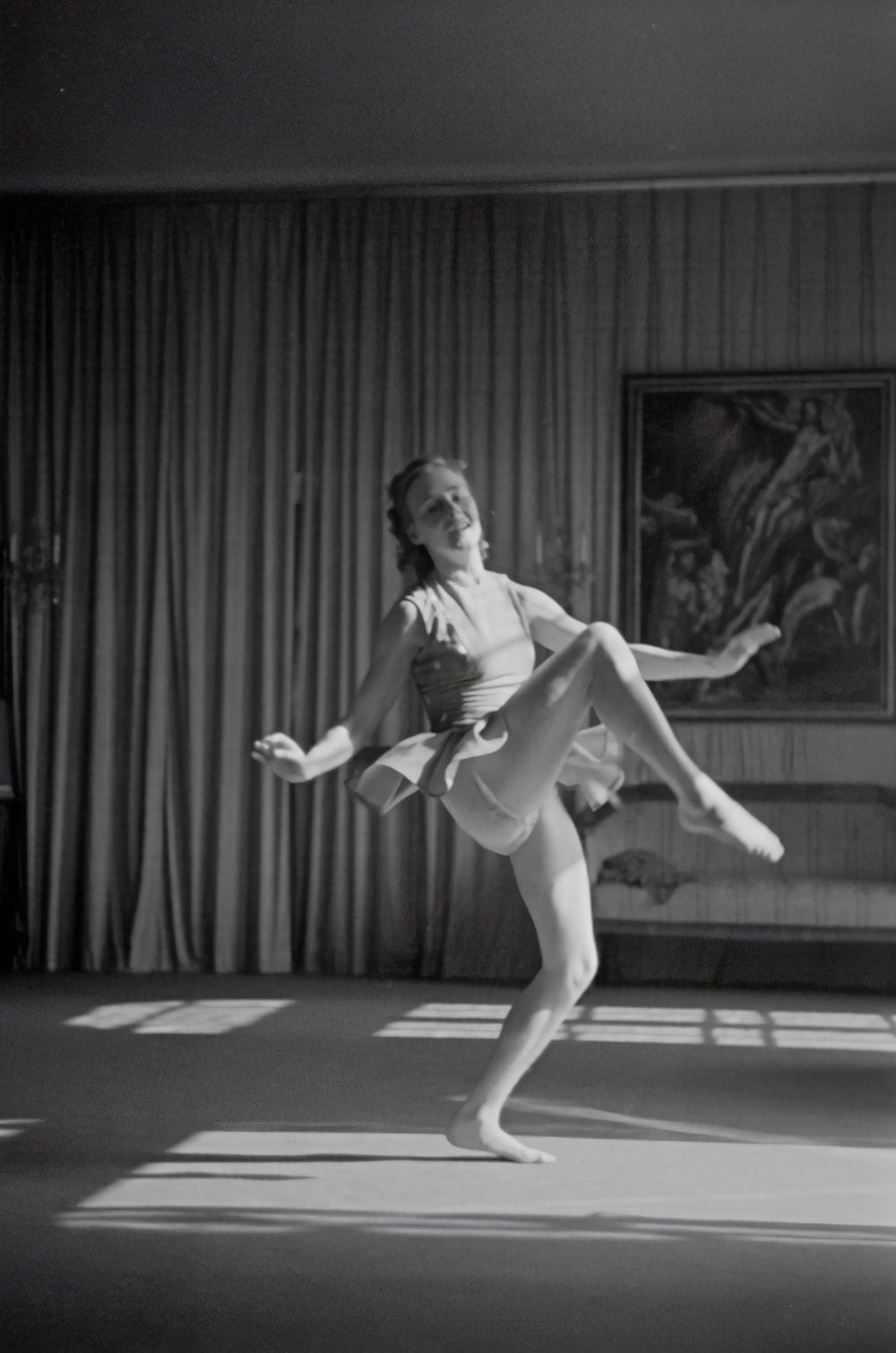 grayscale photo of woman dancing near curtain