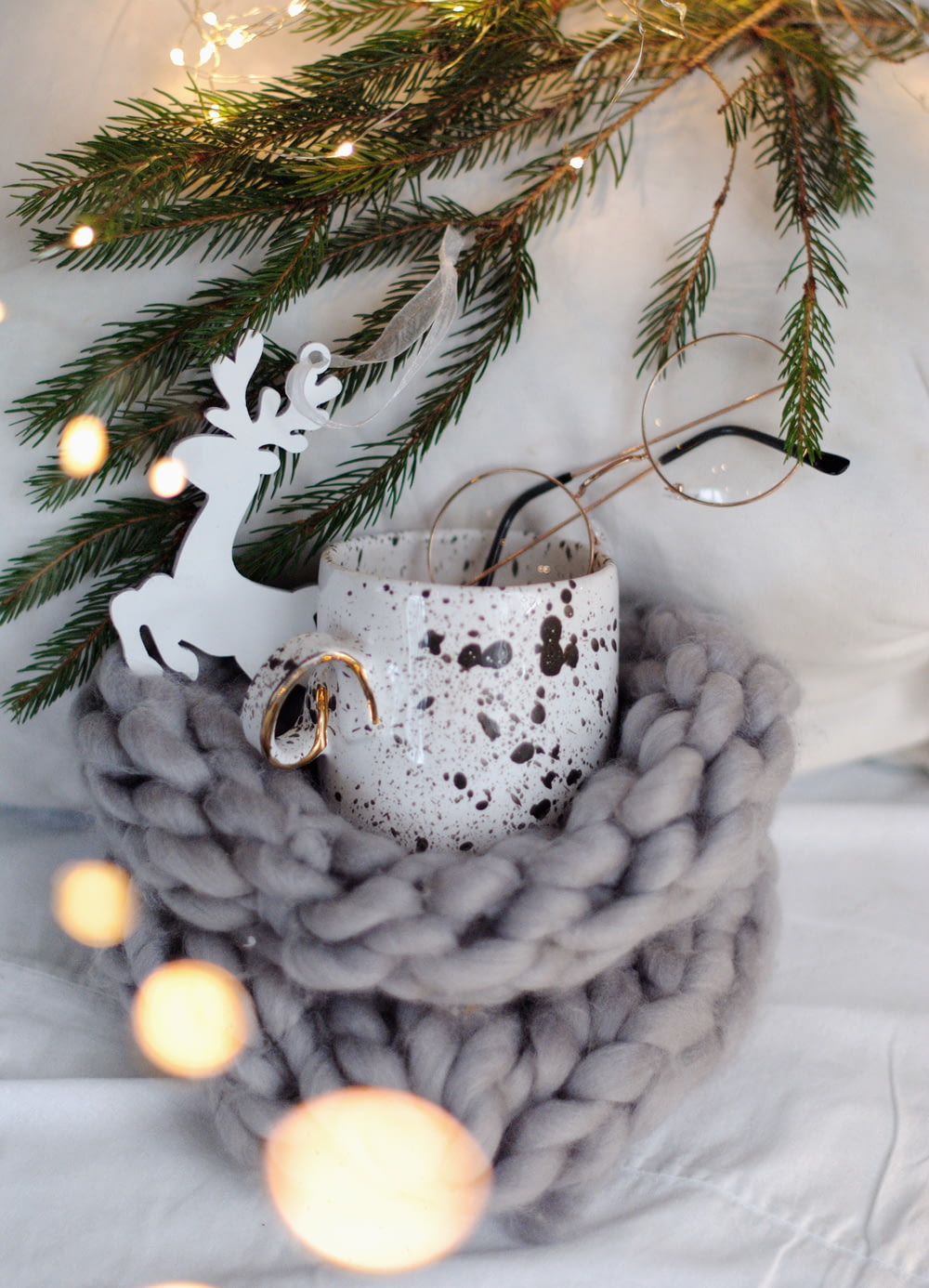 white reindeer decor near white and brown ceramic mug, eyeglasses, and green pine tree