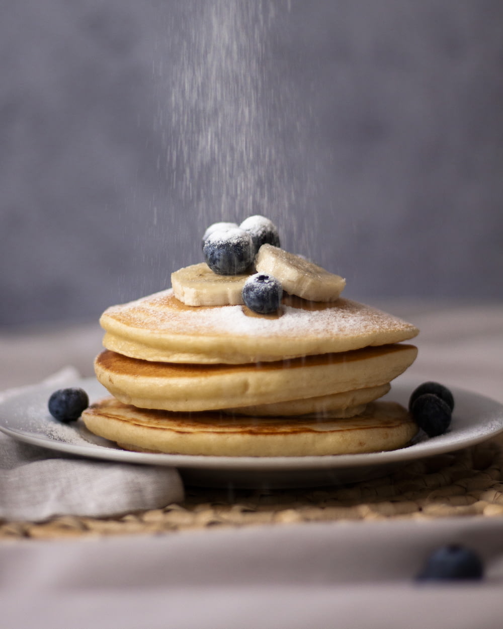 three pancakes with blueberries, sliced banana, and sugar on top