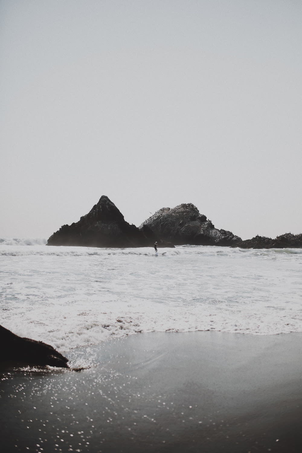 person surfing on beach near rocks