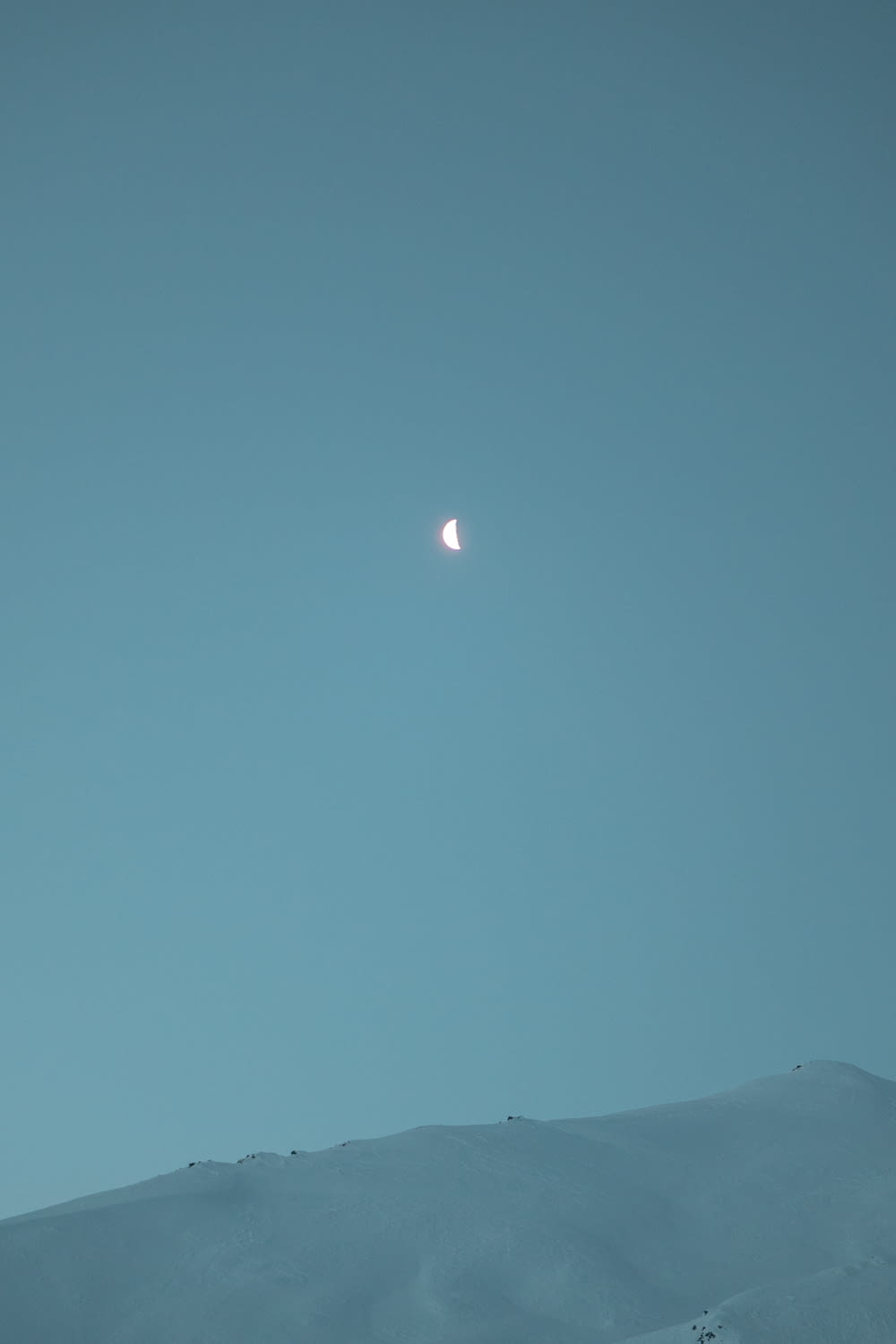 a half moon is seen in the sky above a snowy hill