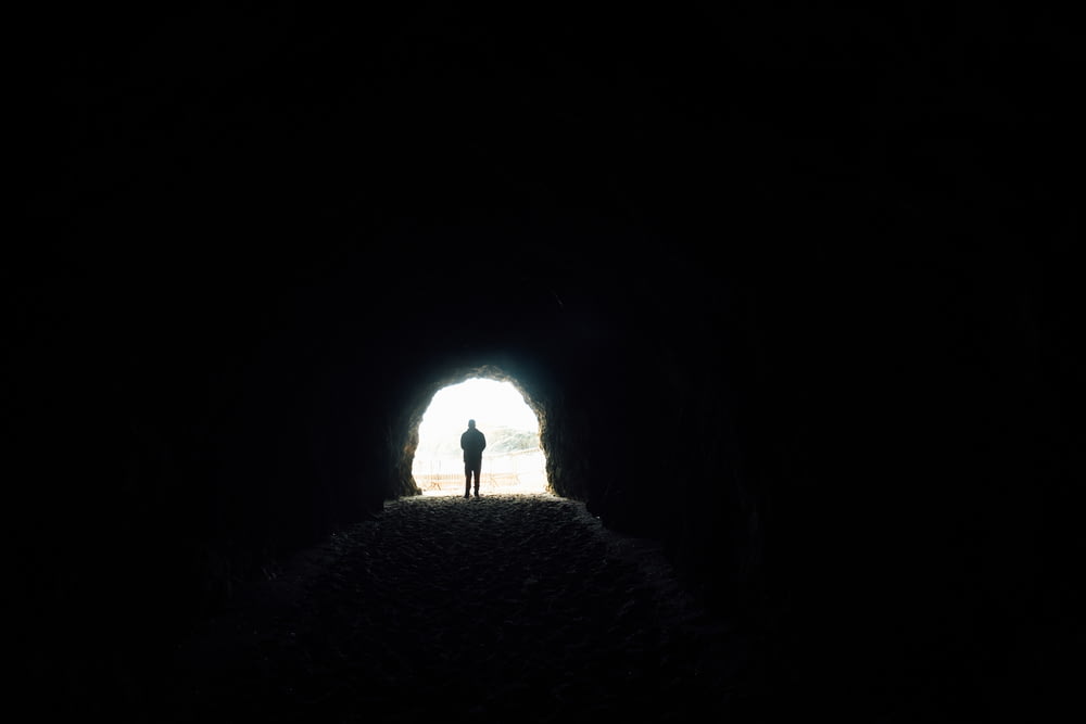 Eine Person, die in einem dunklen Tunnel mit einem Licht am Ende steht