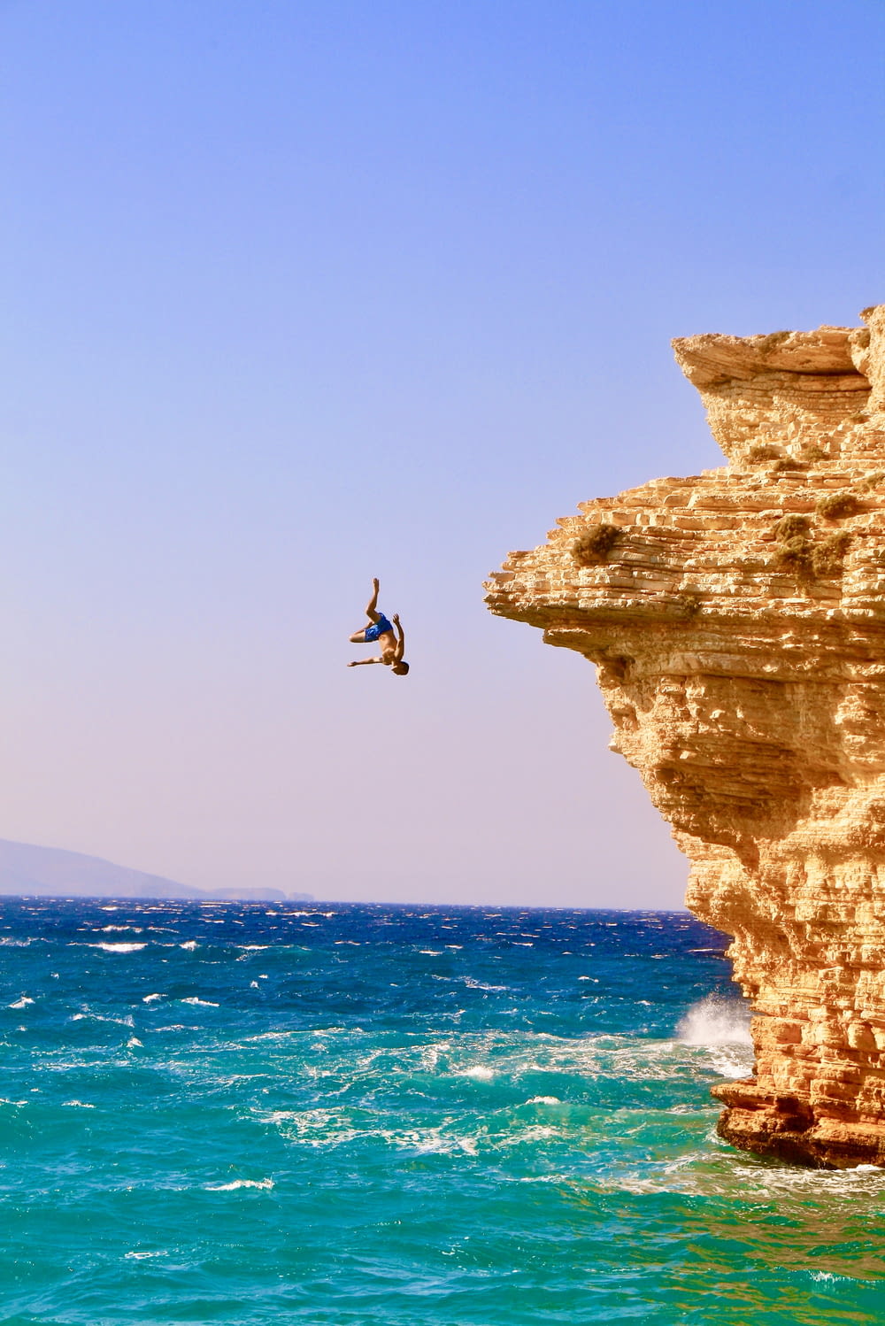topless man jumping from cliff during daytime