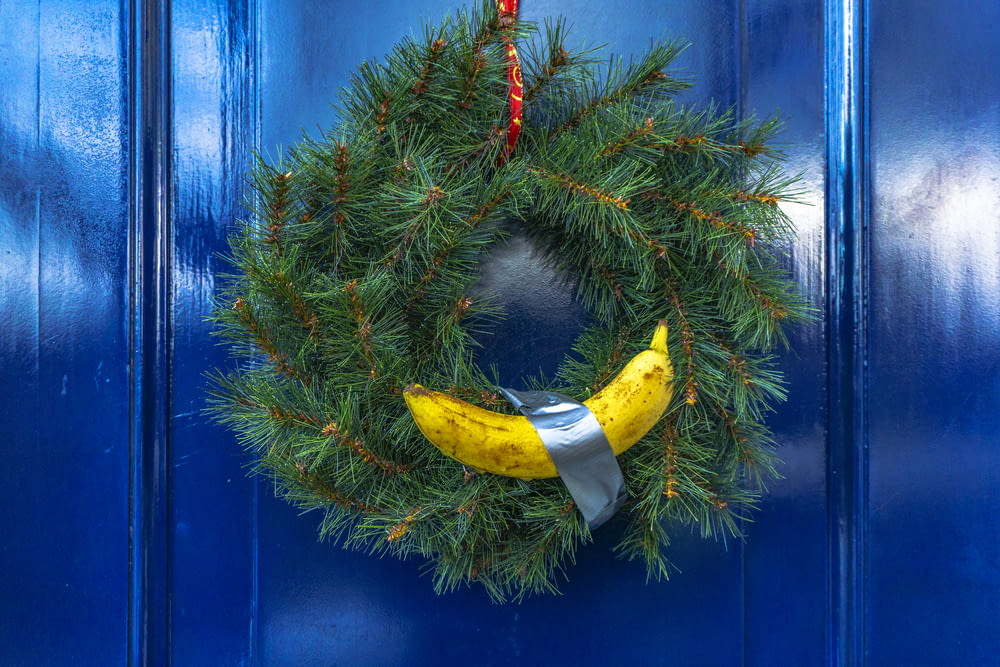 파란색 문에 매달려 있는 노란색 바나나가 있는 녹색 가문비나무 화환