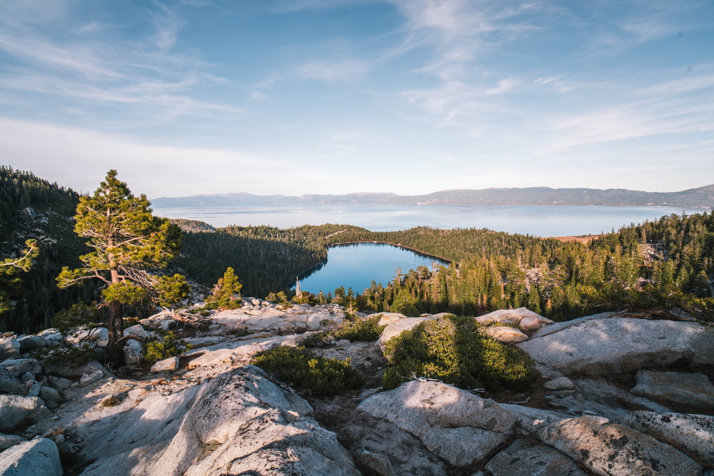 formaciones rocosas que ven el lago rodeado de árboles verdes bajo el cielo blanco y azul