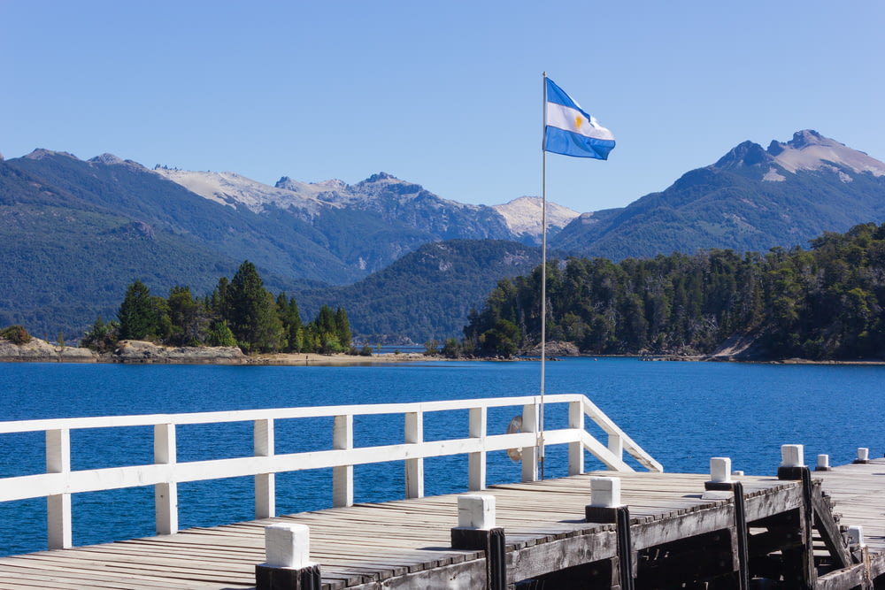 Drapeau blanc et bleu sur un quai en bois près d’un plan d’eau pendant la journée