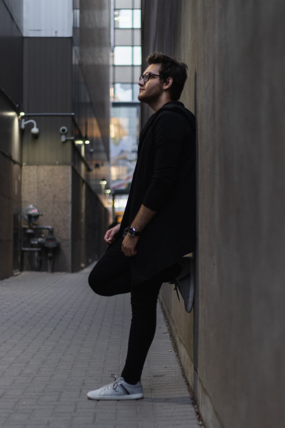 man wearing black jacket standing beside the wall