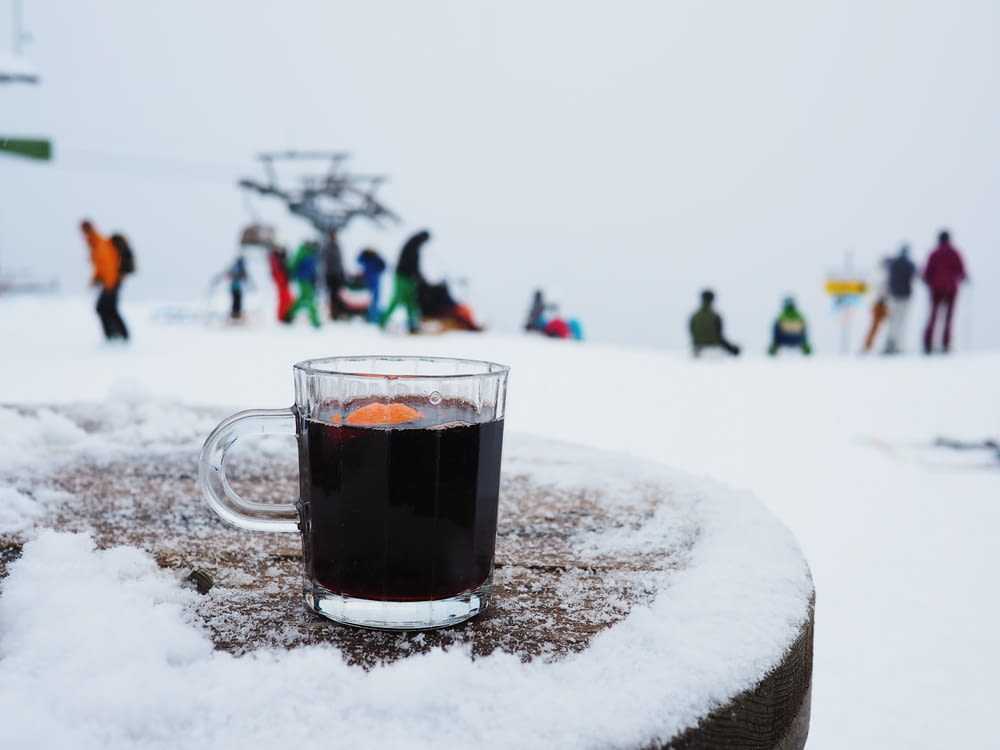 black liquid in clear glass mug and people on snowy field during daytime
