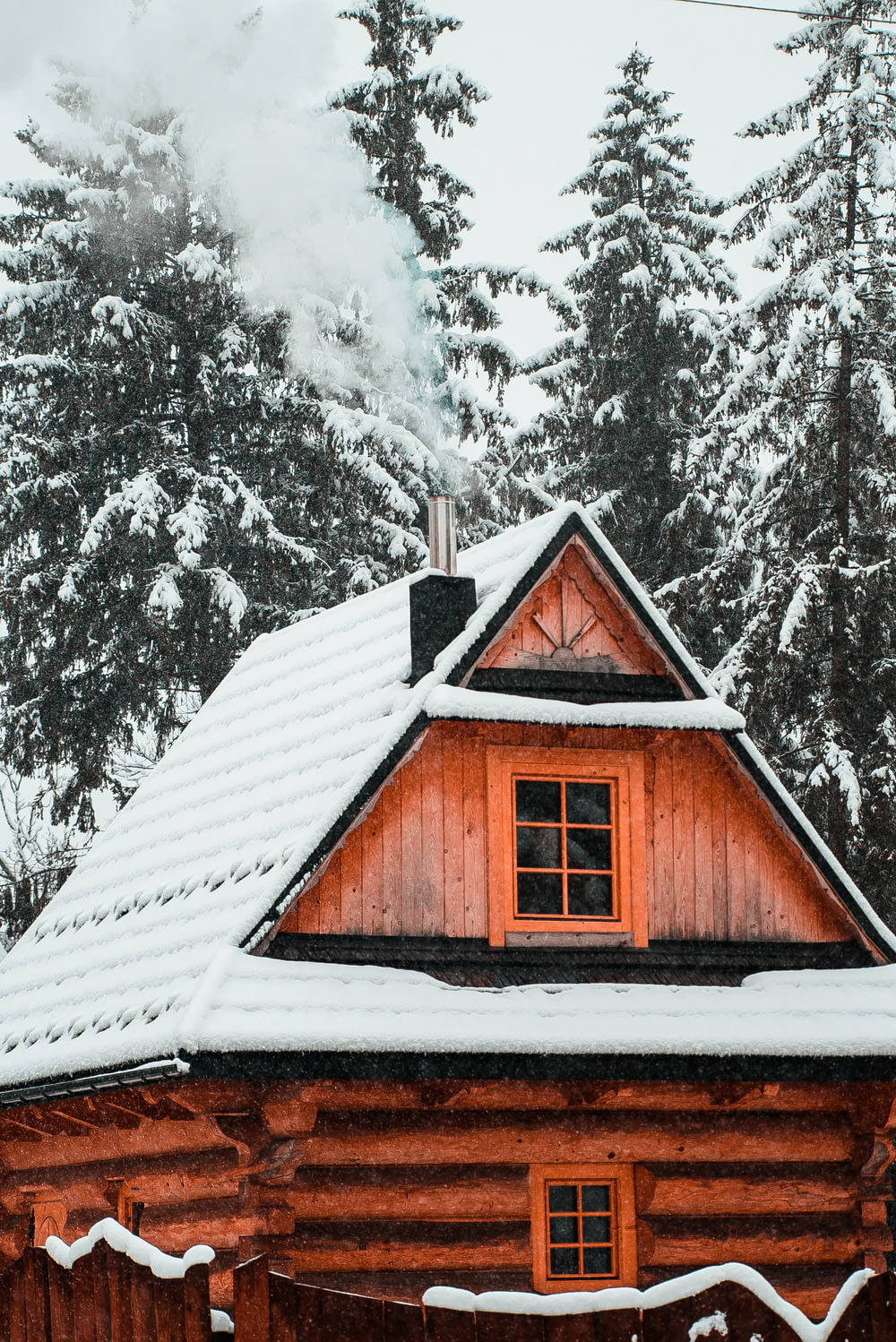 a cabin with snow on the roof and trees in the background