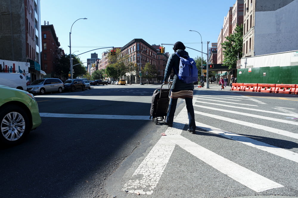 person walking on road while pushing luggage during daytime