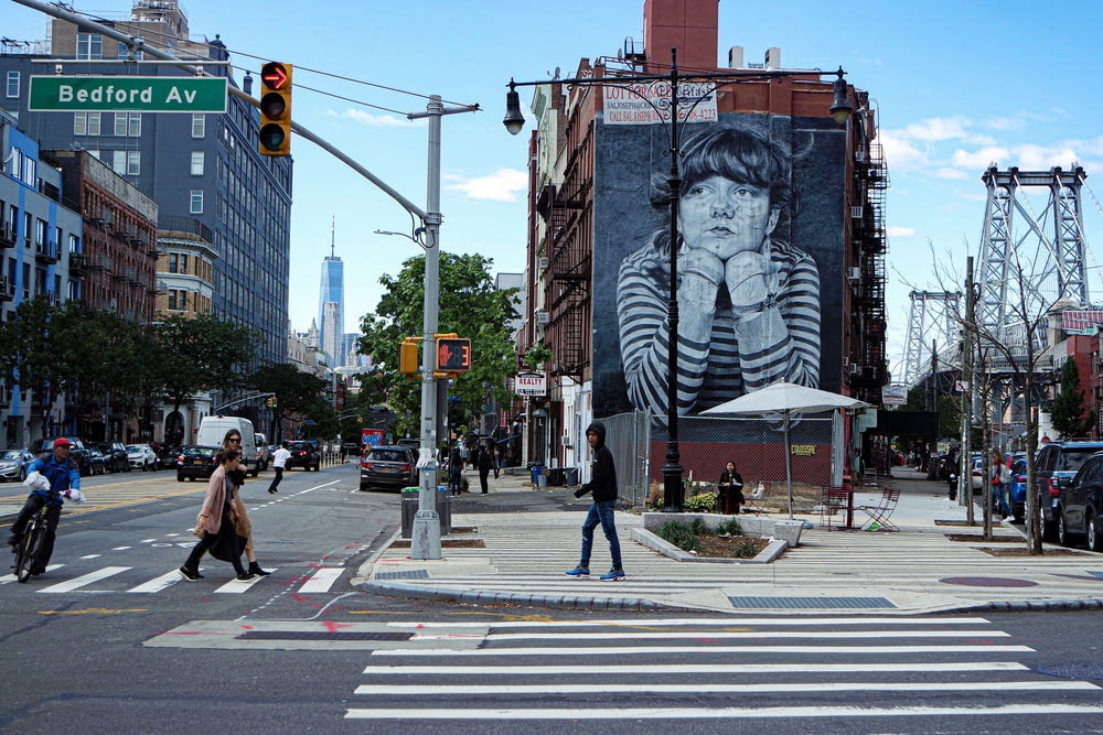 a woman crossing a street in front of a large painting