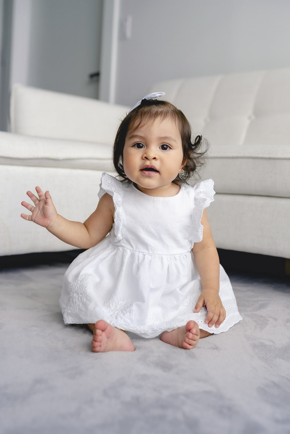 toddler wearing white dress sitting beside white sofa