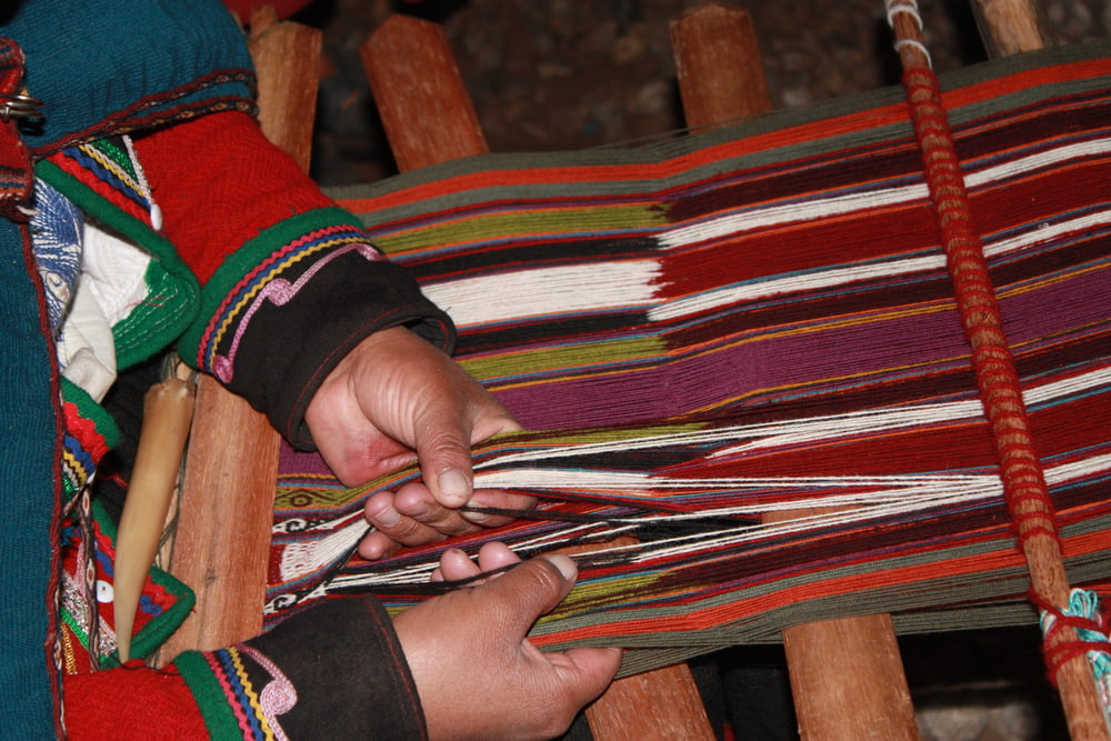 a woman is weaving a colorful blanket on a loom