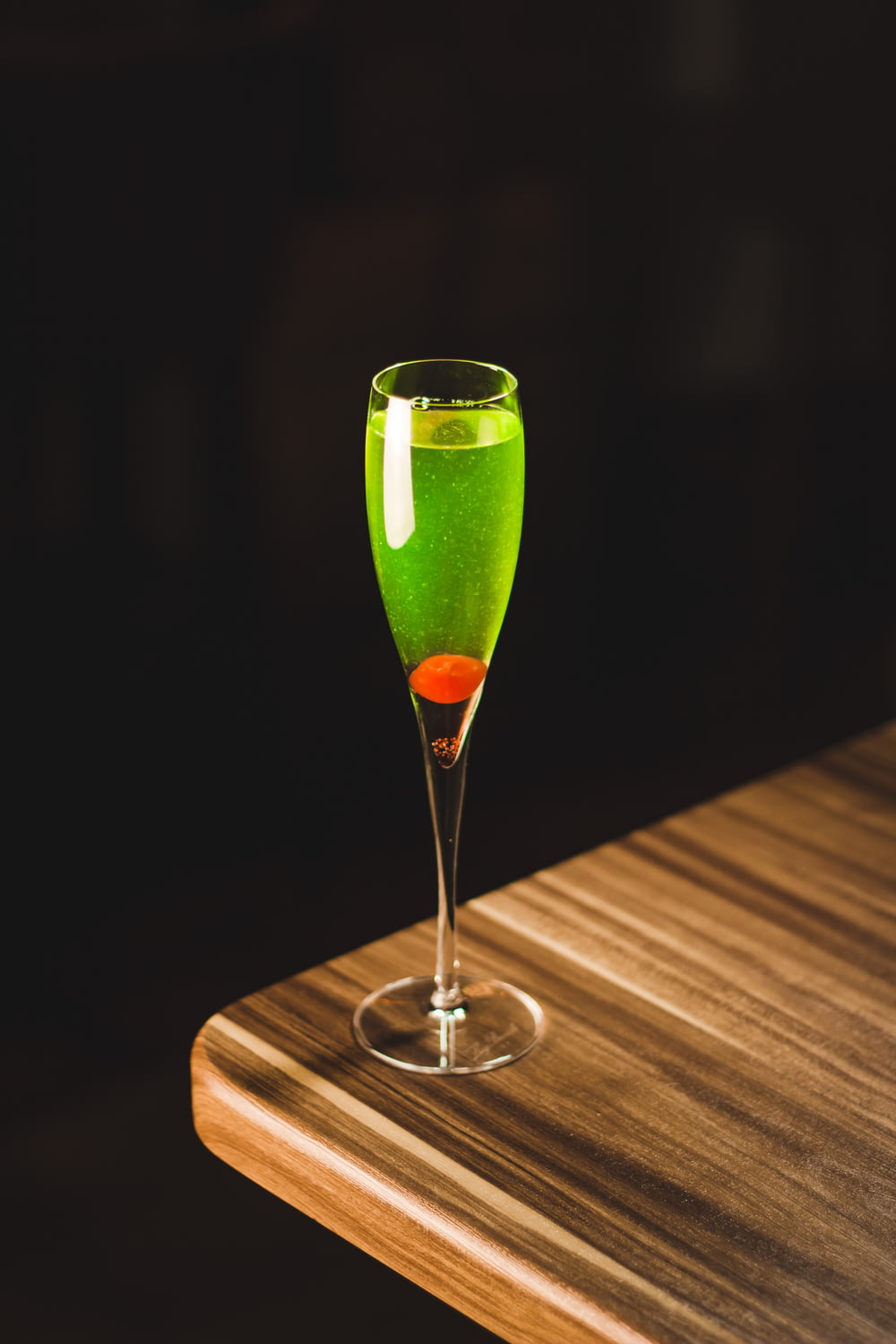 verre tulipe vert rempli de boisson sur le coin de la table en bois