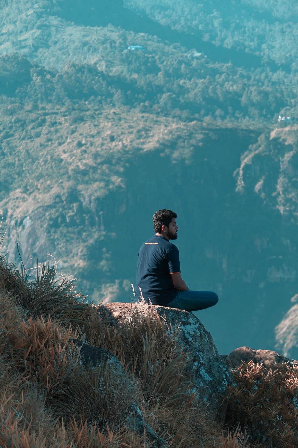 man sitting atop of rock facing mountains at daytime
